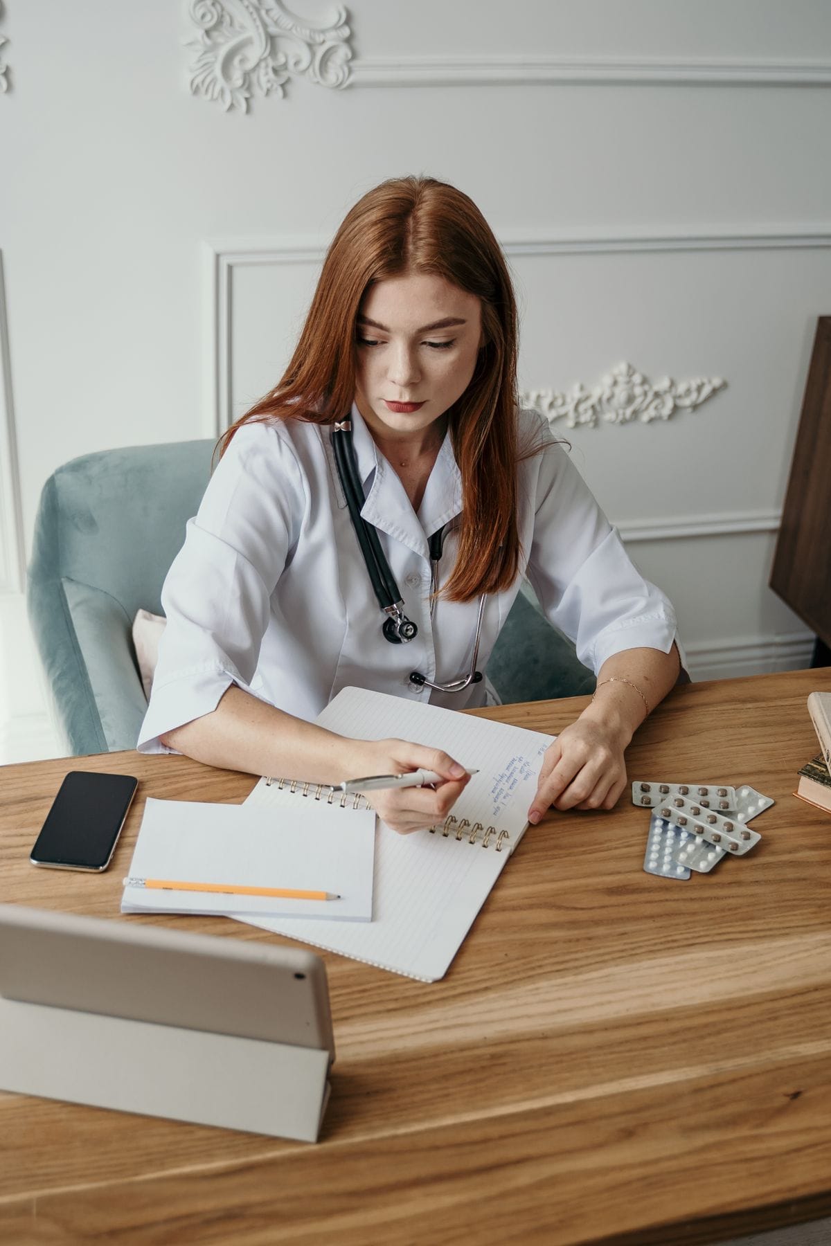 Médica de jaleco e estetoscópio fazendo anotações à mesa do consultório